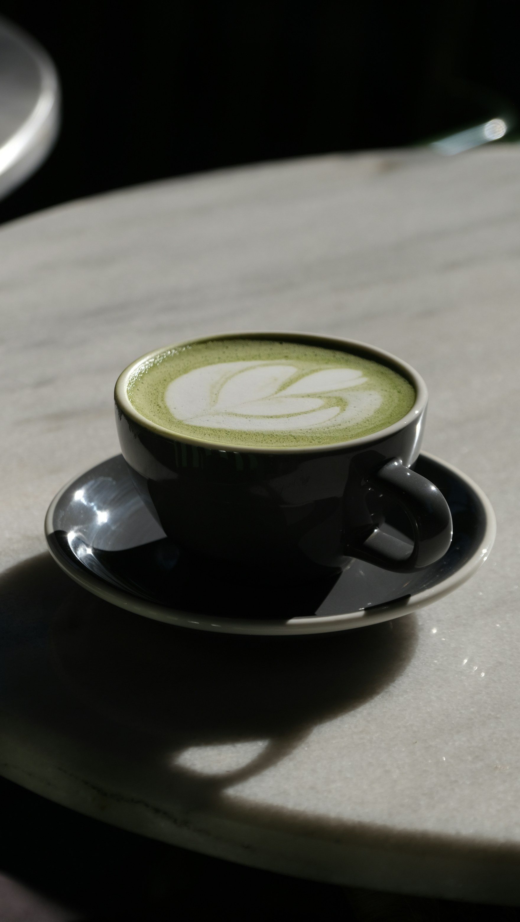 Matcha latte with delicate leaf-pattern latte art in a dark ceramic cup