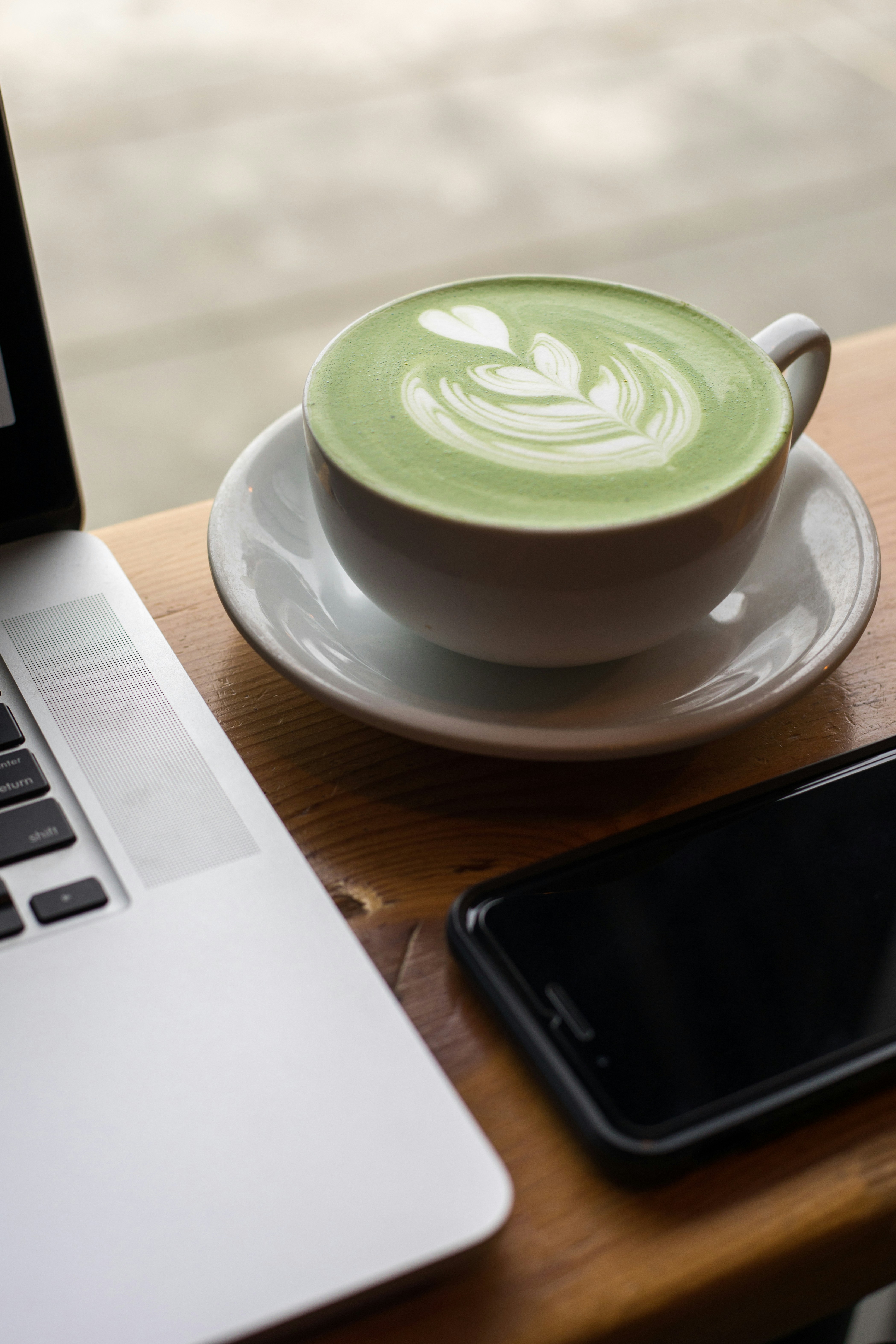 Matcha latte next to a laptop and phone on a work desk