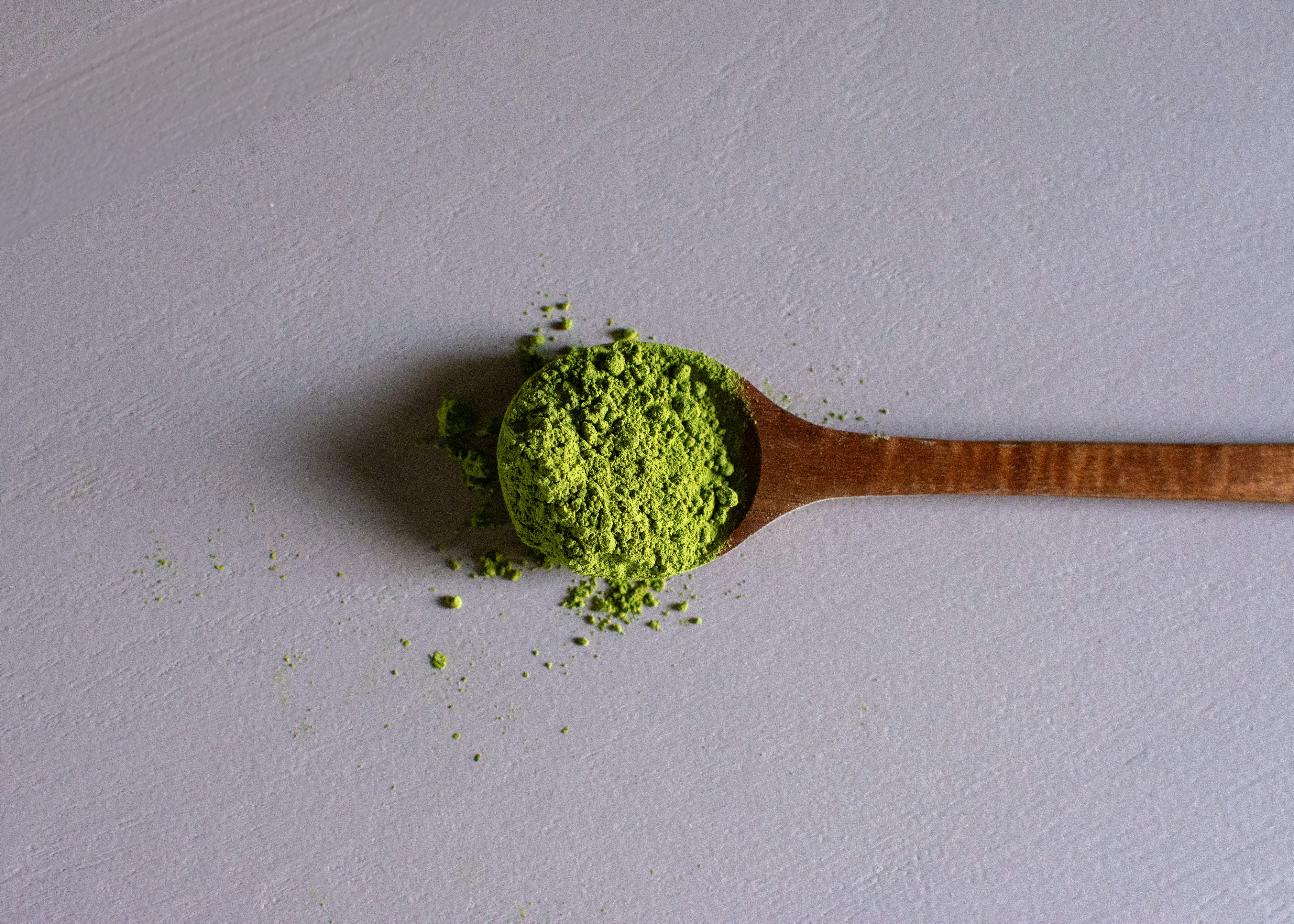 Vivid green matcha powder piled on a wooden spoon