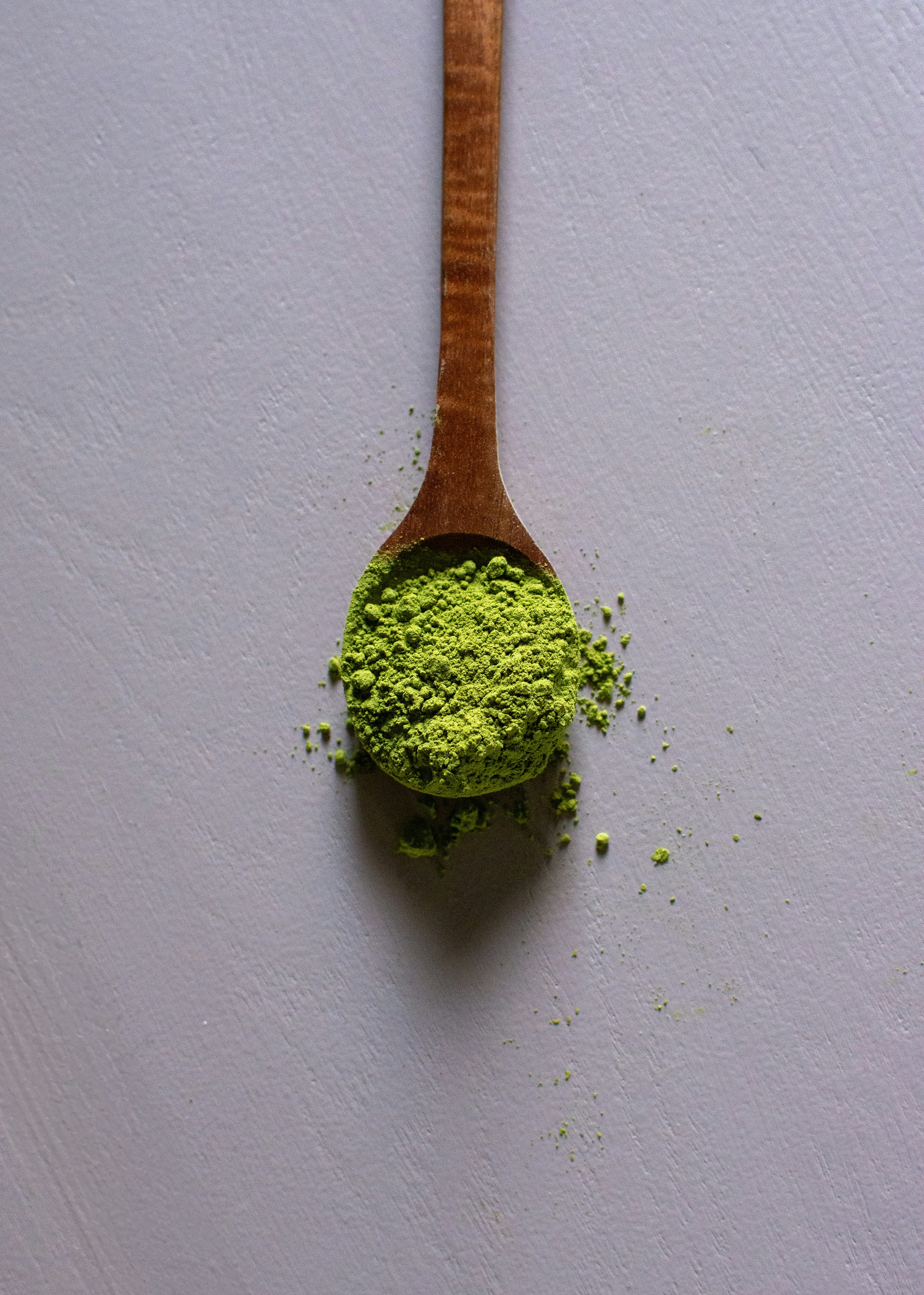 Matcha powder spilling from a wooden spoon
